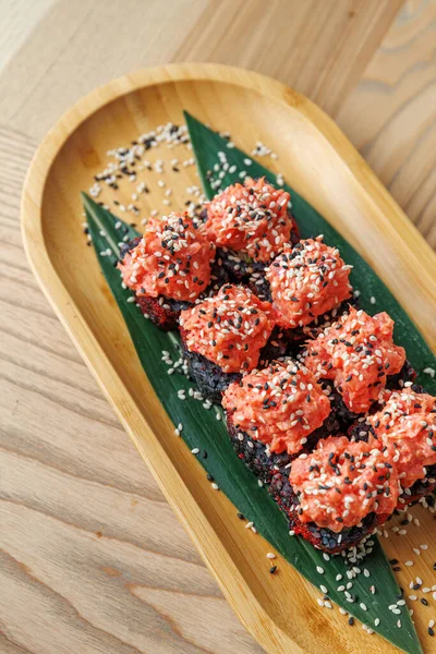 Tabaklarda farklı kültürlerden canlı renklerde çeşitli tatlar sergileniyor. Yemek ahşap bir tepside, yeşil yapraklar ve garnitür olarak serpiştirilmiş susam tohumlarıyla güzelce düzenlenmiş..