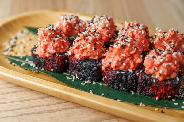 Suşi börekleri kırmızı balık ve siyah susam tohumlarıyla bambu bir tabakta otururlar. Ayarlama sıradan ve davetkar, tipik bir Japon yemek deneyimi..