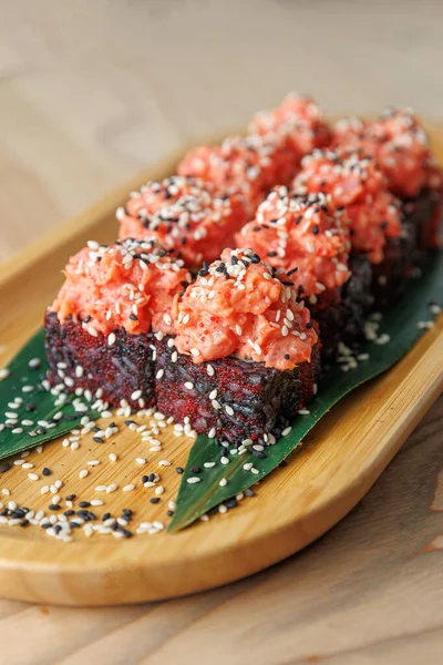 Pembe deniz ürünleri soslu taze suşi ruloları ahşap bir tabakta sergilenir. Ekmekler susam tohumlarıyla süslenip muz yaprağına konuyor. Paylaşım için mükemmel..