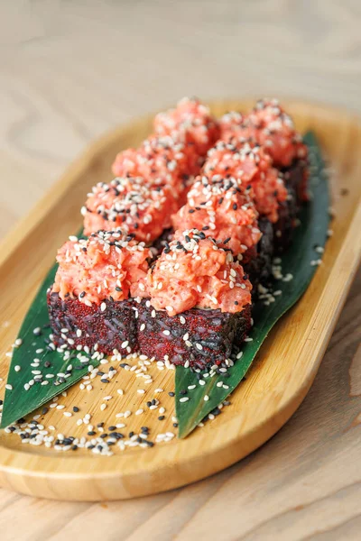 Somonlu, ahşap tepside susam tohumlarıyla kaplı renkli bir suşi düzenlemesi. Yeşil yapraklar sunumu güçlendirir. Gündelik yemek için mükemmel..