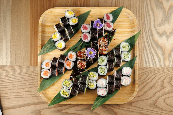 Çeşitli suşi ruloları bambu tabakta düzgünce düzenlenir. Sergide yeşil yapraklar ve küçük çiçeklerle süslenmiş farklı dolgularla renkli rulolar yer alıyor..
