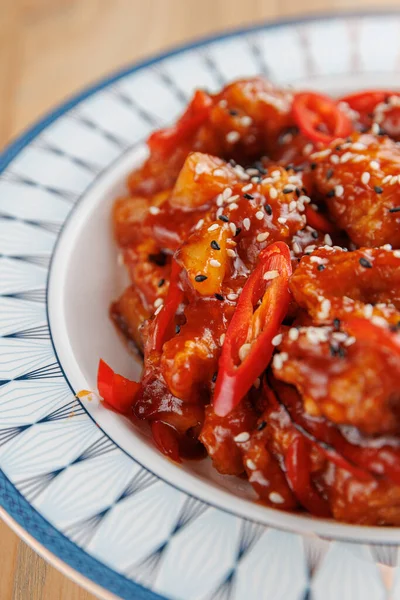 Farklı mutfaklardan bir yemek koleksiyonu sergilenmekte, kırmızı biber dilimleri ve dekoratif bir tabakta susam tohumlarıyla süslenmiş bir tabak baharatlı tavuğun altını çizmektedir..