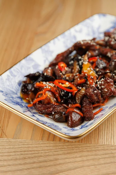 Lezzetli bir yemek sergileniyor. Renkli sebzelerle pişirilmiş, susam tohumlarıyla kaplı taze et parçaları ve dekoratif bir tabakta sunuluyor..