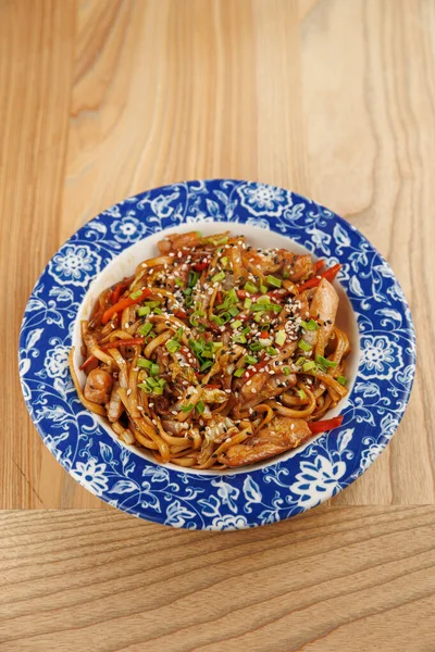 Farklı mutfaklardan gelen çeşitli yemek tabakları ahşap bir masanın üzerindeki renkli bir kaseye konur. Yemekler erişte, sebze, tohum ve düzgün bir şekilde servis edilen etleri içeriyor..