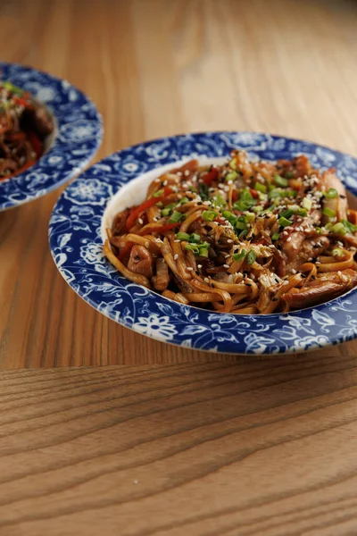 Lezzetli yemeklerden oluşan bir seçimde Ukrayna ve Japonca gibi çeşitli mutfaklar sergileniyor. Ahşap bir yüzey üzerinde desenli kaselerde servis edilen otlarla kaplı renkli erişteler..