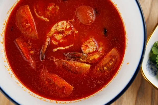 İçi deniz ürünleri, domates ve diğer sebzelerle dolu bir kase ahşap bir masada duruyor. Taze otlar, küresel mutfaklardan çeşitli tatlar sunan tabağa eşlik ediyor..