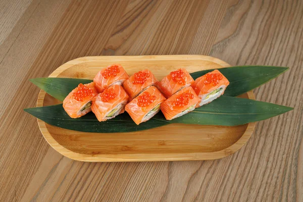 Taze somon ve yumurtayla dolu suşi ruloları bambu yaprağı tabağında güzelce sıralanır. Bu yemek Japon mutfağını temsil ediyor ve bir yemek masasında servis ediliyor..