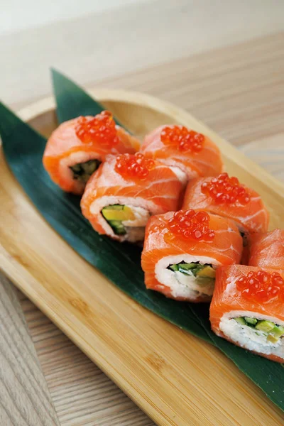 Sebze ve deniz ürünleriyle dolu suşi ruloları dikkatlice ahşap bir tabağa konur. Parlak turuncu somon balığı ve parlak kırmızı yumurta her rulonun üstünde renkli bir yemek oluşturur..