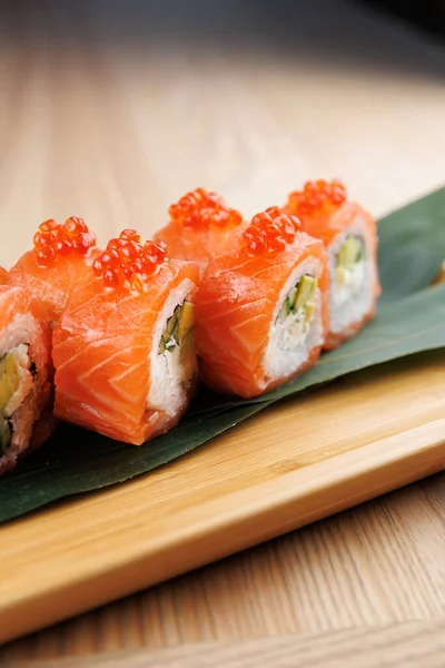 Somon, balık yumurtası ve sebzelerden yapılmış suşi ruloları ahşap bir tabakta oturur. Alttaki yeşil yaprak suşinin sunumunu güçlendirir..