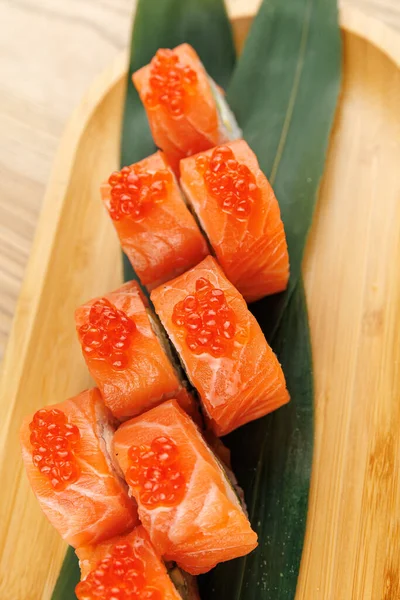 Parlak turuncu yumurtayla kaplanmış somon balığı parçaları ahşap bir tabağa yerleştirilmiş yeşil bir yaprağa yerleştirilmiş ve bir yemek masasında canlı bir yemek sunumu sergilenmektedir..