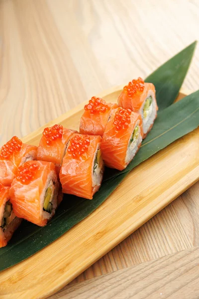 Tabaklar somon balıklı suşi ruloları ve bambu kabının üzerinde balık yumurtası ile doludur. Dekorun hafif ahşap bir yüzeyi var, Japon mutfağından zevk almak için mükemmel..