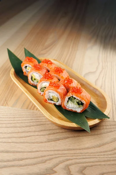 Ahşap bir tabakta salatalık ve somon ve turuncu yumurtayla doldurulmuş birden fazla suşi ruloları bulunur. Doğal ahşap yüzeyi, rahat bir yerde yemek deneyimine katkı sağlar..
