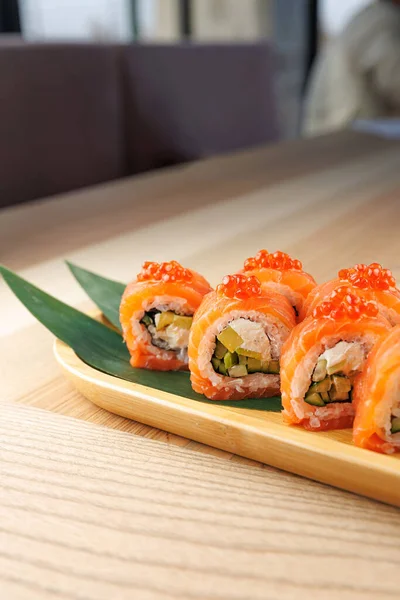 Taze malzemeli renkli suşi ruloları ahşap bir tabakta güzelce düzenlenir. Rulolarda somon, sebze ve portakal balığı yumurtası var..