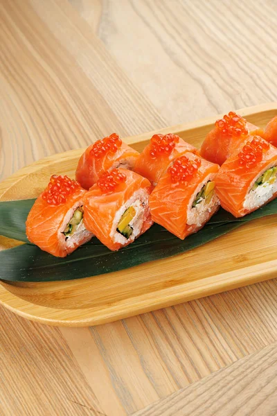 Somon, avokado ve havyardan yapılan taze suşi ruloları ahşap bir tabakta sunulur. Bu yemek malzemelerin canlı renklerini ve dokularını gösteriyor..