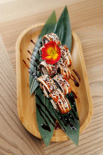 Suşi ruloları, yapraklı ve canlı bir çiçekli bambu bir tabakta ustalıkla düzenlenir. Sos yağmuru sunuma karşıtlık ekler.