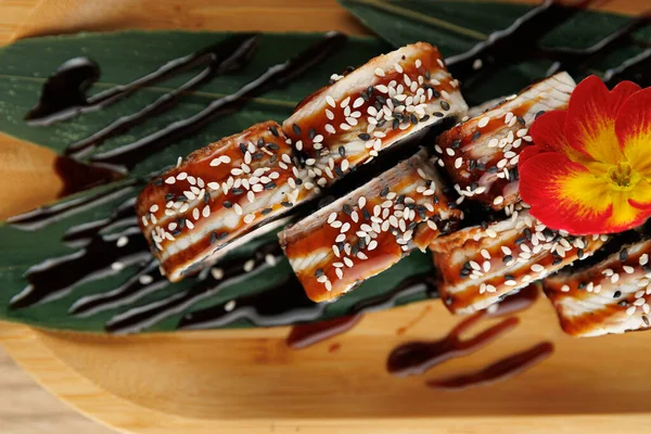 Suşi ruloları bambu tabakta güzelce düzenlenir. Susam tohumlarıyla süslenmiş ve sosla ıslatılmışlar. Bir çiçek sunuma renk ekler.