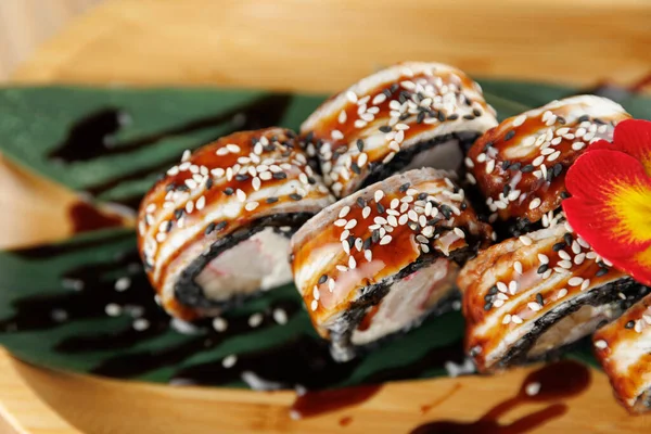 Üzerine yılan balığı sosu ve susam tohumları serpiştirilmiş suşi ruloları bir yaprağın üzerinde servis edilir. Bu yemek, bir restoran ortamında Japon mutfağının unsurlarını ön plana çıkarıyor..