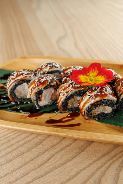 Pirinç, deniz yosunu ve çeşitli dolgulardan yapılan suşi ruloları bambu tabağında güzelce sıralanır. Renkli bir çiçek tabağa dekoratif bir dokunuş ekler..