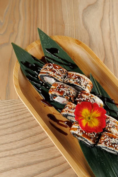 Suşi hamuru, yeşil yapraklı ve kırmızı çiçekli ahşap bir tabakta güzelce sıralanmış. Tabakta zengin bir sos ve Japon mutfağından bir tat karışımı sergileniyor..