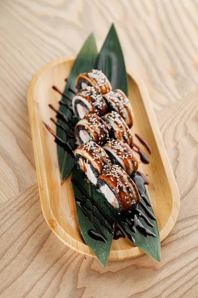 Suşi ruloları yeşil yapraklar üzerinde güzelce düzenlenir ve ahşap bir tabakta servis edilir. Kara sos çiselemeleri, sıradan bir restoranda yemeğin sunumunu güçlendirir..