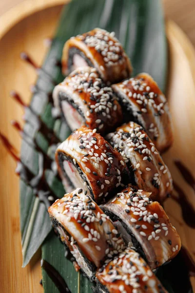 Suşi rulolarında yılan balığı ve susam bir bambu tabağına oturur. Sunumda lezzet artırıcı yeşil yapraklar ve bir tutam sos yer alıyor..