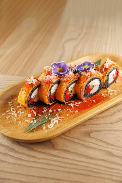 Suşi hamuru ahşap bir tabakta düzgün bir şekilde dizilmiş. Lezzet ve renklerin karışımını gösteriyor. Başlıklar arasında yenilebilir çiçekler ve hoş kokulu otlar yer almakta olup, restoranlar için sunumun geliştirilmesi.