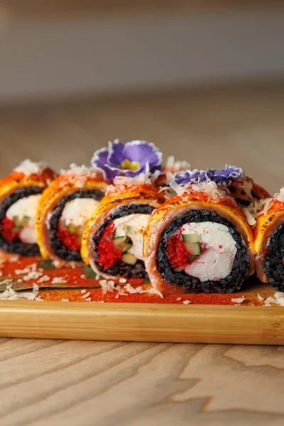 Tahta bir tahtanın üzerinde düzenlenmiş canlı dolgu ve malzemeler içeren bir suşi rulosu seçimi. Ekmekler taze malzemeler içeriyor ve dekorasyon için yenilebilir çiçeklerle süsleniyorlar..