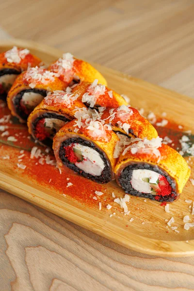 Suşi dürümleri ahşap bir tabakta, canlı renkler ve dokular sergiliyor. Taze sebzeler ve lezzeti artırmak için malzemelerle süslenmiş deniz ürünleri..