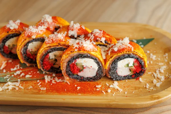 Suşi ruloları ahşap bir tabakta güzelce düzenlenir. Her rulo çeşitli malzemelerle ve renkli süslemelerle dolu. Ortam sıcak ve davetkar görünüyor..