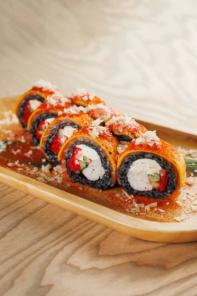 Suşi börekleri yengeç, salatalık ve baharatlı sos gibi çeşitli malzemeler içerir. Ahşap bir tabakta servis edilir, malzemelerle süslenir, yemek için mükemmeldir..