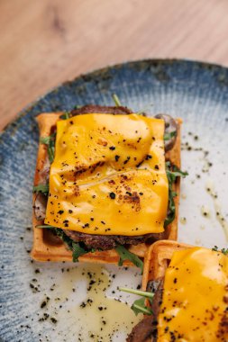 Ağız sulandıran waffle sandviçi eritilmiş peynir, taze yeşillikler ve baharatlar içerir. Bu yemek her yemek için mükemmel bir lezzet karışımı sunar. Lezzetli kombinasyonun tadını çıkar.