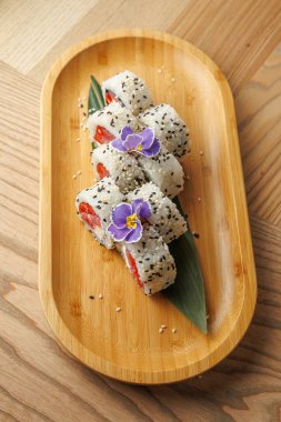 Pirinç ve balıktan yapılan suşi ruloları ahşap bir tepside düzenlenir. Bu tabakta susam tohumları ve garnitür için yenebilir çiçekler var. Japon mutfağı sergileniyor..