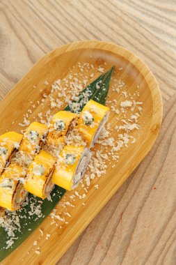 Suşi börekleri rendelenmiş hindistan ceviziyle kaplı bir bambu tabağında yeşil bir yaprağa konur. Ayarlar Japon yemeklerinde yaygın olan basit bir ahşap masayı gösteriyor..