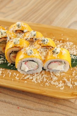 Suşi ruloları ahşap bir tahtanın üzerinde düzenlenir. Ekmekler yengeç, krem peynir ve çeşitli süslemelerle kaplıdır. Bu ayar sıradan bir yemek deneyimi sunuyor..