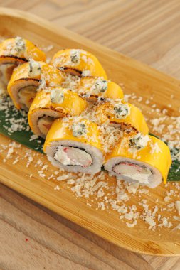 Suşi ruloları ahşap bir tabakta, canlı renkler ve dokular sergilenerek güzelce düzenlenir. Bu yemek Japon mutfak sanatını yansıtan malzemelerin karışımını vurgular..