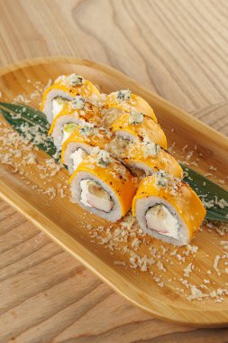 Renkli suşi ruloları ahşap bir tabakta güzelce düzenlenir. Toptancılar ve garnitürler görsel cazibeyi arttırır. Dinleyicileri bu lezzetli Japon yemeğinin tadını çıkarmaya davet eder..