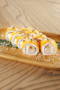 Suşi ruloları ahşap bir tabakta servis edilir. Yemek, günlük yemek ortamında soslarla süslenmiş yengeç eti, avokado ve peyniri içeriyor..