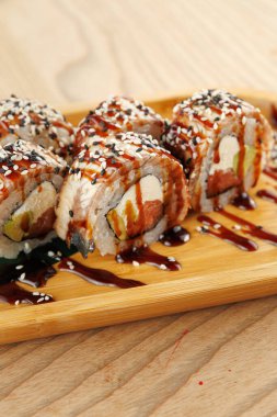 Renkli suşi dürümleri ahşap bir tahtada güzelce düzenlenir. Her rulo deniz ürünleri, sebzeler ve soslardan oluşan bir karışım içermekte ve davetkar bir yemek seçeneği sunmaktadır..