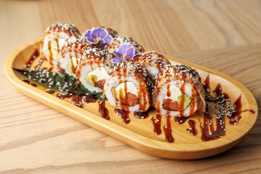 Suşi ruloları ahşap bir tabakta güzelce düzenlenir. Yemek malzemeler, soslar ve süsleri içeriyor. Geleneksel Japon yemekleri bir restoranda sergileniyor..