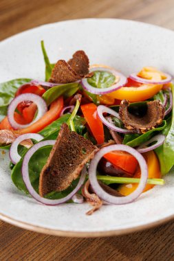 Taze salatada ıspanak, dilimlenmiş dolma biber, kırmızı soğan ve çıtır ekmek cipsi bulunur. Yemek, sıradan bir yemek ortamında yuvarlak bir tabakta sunuluyor..