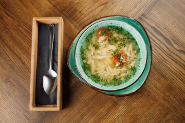 Bir kase Ukrayna çorbası ahşap bir masada duruyor. Çorbada lahana, domates ve otlar var. Tahta servis kutusu ve kaşık kasenin yanına konur, kullanıma hazır..