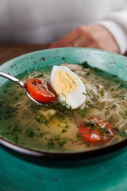 Bir insan Ukrayna borşundan dilimlenmiş yumurta ve vişneli domatesle keyif alır. Çorba taze dereotuyla süslenir, tabağa tat katar..