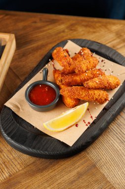 Yuvarlak bir tabakta, üzerinde bir kase sos ve ahşap bir yüzey üzerinde limon dilimi olan bir kağıt üzerinde kızarmış atıştırmalıklar..