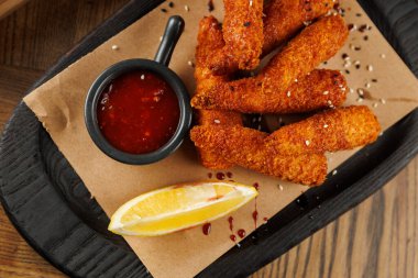 Pişmiş atıştırmalıklar ahşap bir tabakta küçük bir kase sos ve bir dilim limon ile güzelce düzenlenir. Ayarlar rahatlamış bir yemek deneyimi olduğunu gösteriyor..