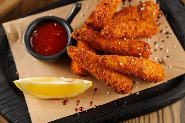 Kızarmış atıştırmalık bir porsiyon, küçük bir kase kırmızı sos ve ahşap bir tabakta limon dilimi ile güzelce düzenlenir. Bu yemek her yemek için nefis bir seçim sunar..