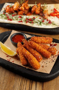 Kırmızı sos ve limon dilimiyle servis edilen kızarmış atıştırmalıkların yanında sebzeli ızgara tavuk. Tabaklar paylaşmak için ahşap bir masada sunuluyor..