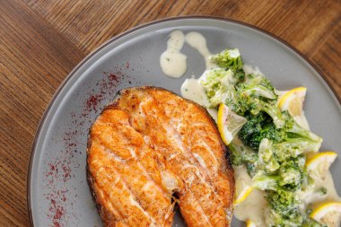 Baharatla süslenmiş ızgara somon filetosu yemek tabağında kremalı sosla serpiştirilmiş brokolinin yanında oturur..