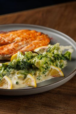 Krem soslu ve limon dilimleriyle süslenmiş buharda pişirilmiş brokoli ile birlikte pişirilmiş somon fileto. Bu yemek öğle veya akşam yemeği için uygundur..