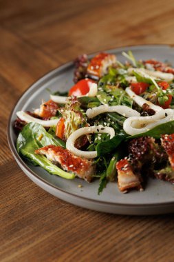 Taze salata çeşitli sebzeler, ızgara tavuk parçaları, kiraz domatesleri ve gri bir tabakta susam tohumları. Hafif bir yemek için mükemmel bir seçenek..