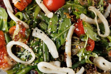 Renkli bir salatada taze yeşiller, kiraz domatesleri ve yumuşak mürekkep balığı halkaları bulunur. Sıradan bir restoranda hafif bir öğle yemeği ya da akşam yemeği için uygun bir kasede servis edilir..